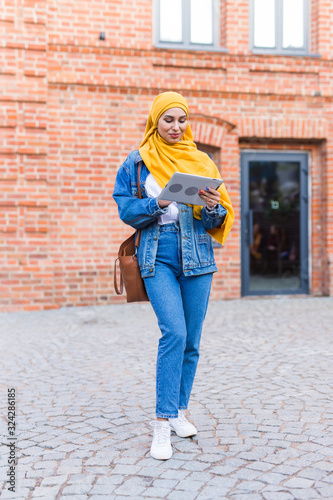 Arab woman student. Beautiful muslim female student wearing bright yellow hijab holding tablet.