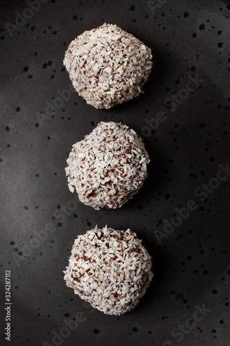 Homemade natural energy ball with coconut shavings on a plate and a light marble background. Gluten free. Top view. 