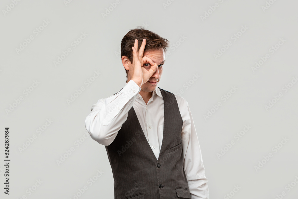 Handsome young man in a white shirt and grey vest opens eye to see better Handsome young man in a white shirt and grey vest opens eye to see better