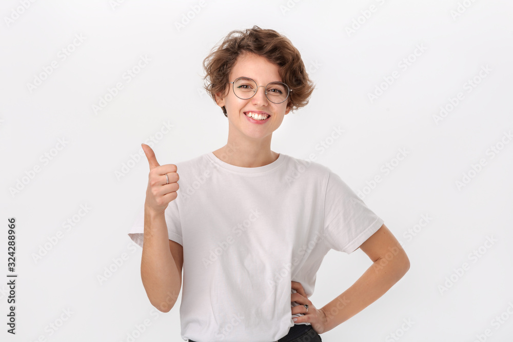 Pretty smiling woman in white shirt and eyeglasses holding thumb up to express appreciation Pretty smiling woman in white shirt and eyeglasses holding thumb up to express appreciation