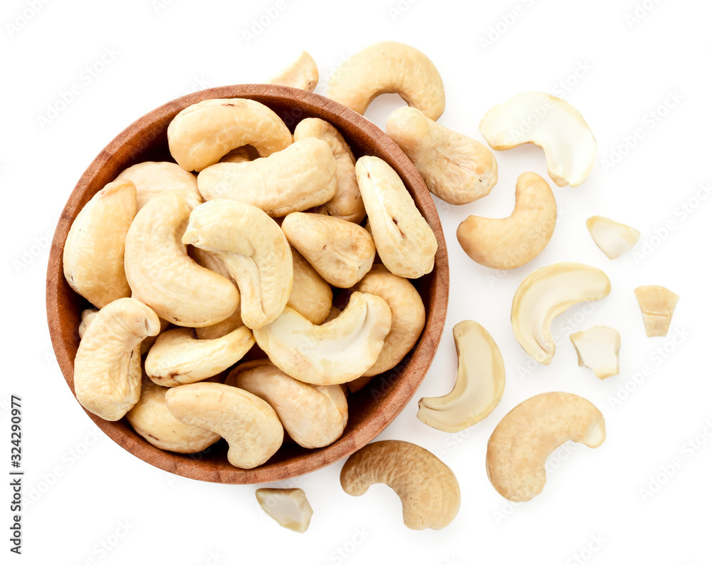 Cashew nuts in a wooden plate and scattered on a white background. View from the top Cashew nuts in a wooden plate and scattered on a white background. View from the top