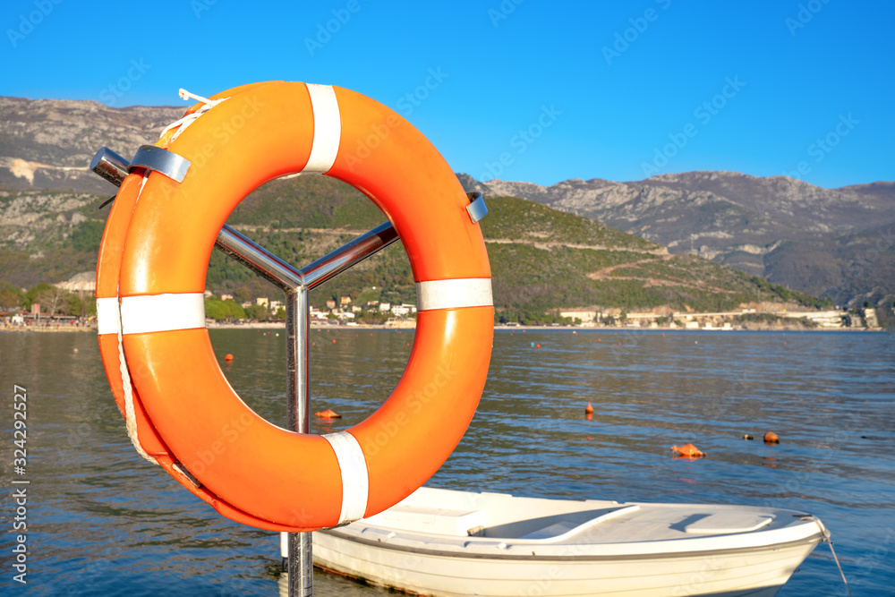 Closeup orange lifebuoy on a background of a boat in a marina swinging on the waves in the sea on a bright sunny day