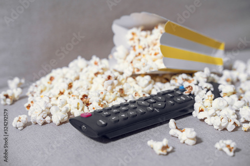 The cardboard box with popcorn and remote control on grey background. Concept of hobby or pleasant time spending at home, watching movie. Indoors.