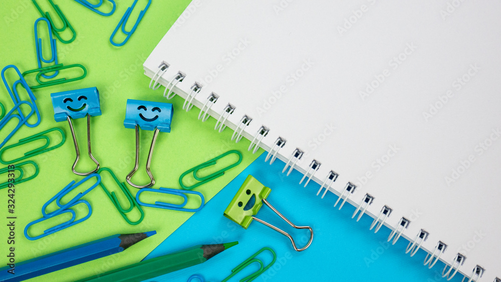 Green and Blue Office Paper Clip, Smile Binder Clips and Pencils on Notepad. Office supplies on Green and Blue Background. Open spiral notebook on table. Knowledge or education. Back to school Green and Blue Office Paper Clip, Smile Binder Clips and Pencils on Notepad. Office supplies on Green and Blue Background. Open spiral notebook on table. Knowledge or education. Back to school