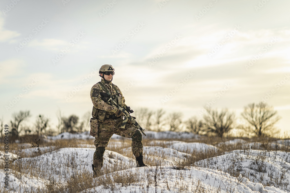 Fototapeta premium equipped army soldier Man in the winter khaki camouflage is patrolling or patrol field territory. commandos with full equipment helmet and gun watch battlefield. Modern army soldier
