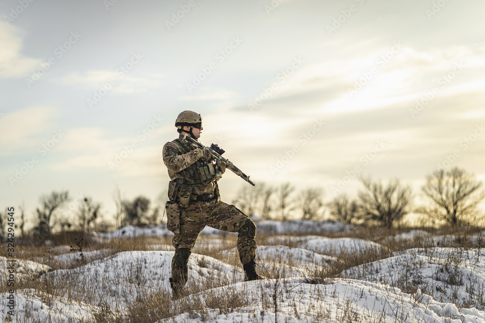 equipped army soldier Man in the winter khaki camouflage is patrolling or patrol field territory. commandos with full equipment helmet and gun watch battlefield. Modern army soldier