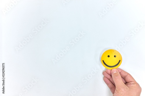 A hand holding a yellow happy face in white background with copy space. Positive customer feedback and review. Happiness and Good service concept. photo