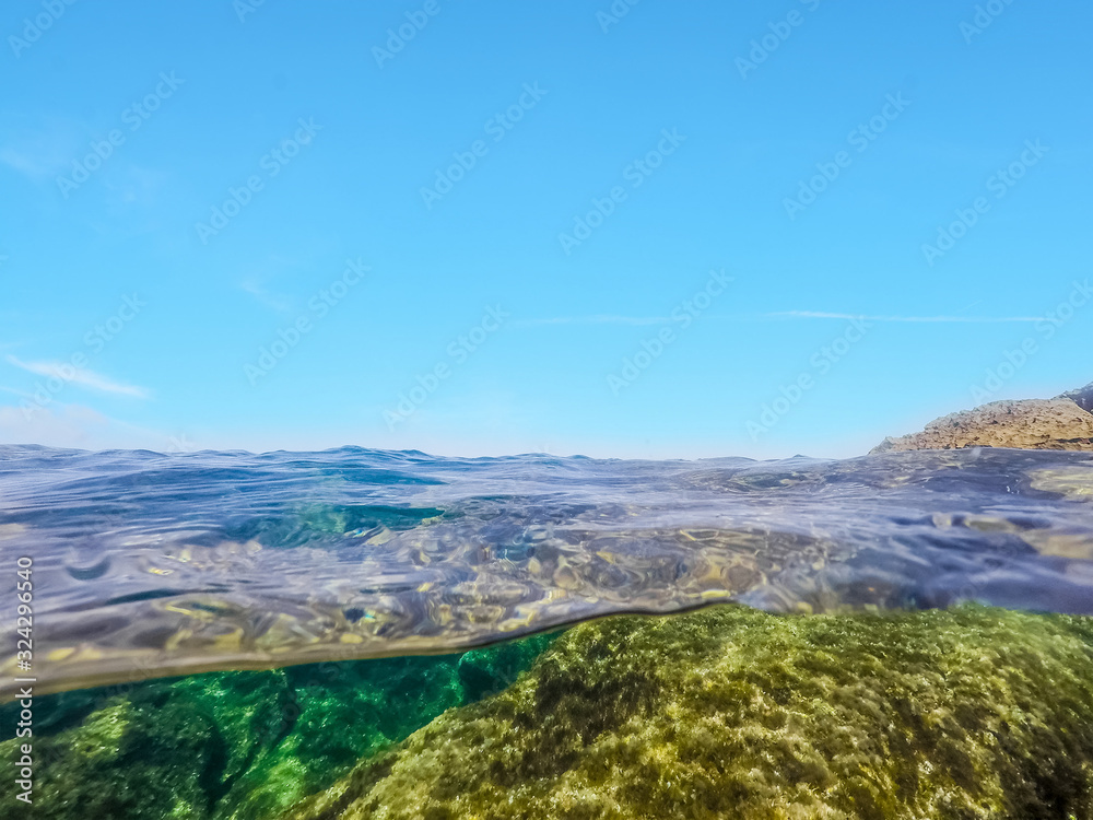Split underwater view of rocks under the sea and blue sky in Alghero