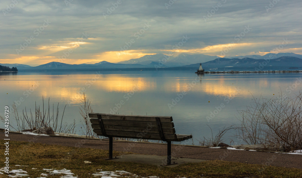 bench on Lake Champlain water front with view of vibrant sunset and the New York Adirondack mountains in winter 