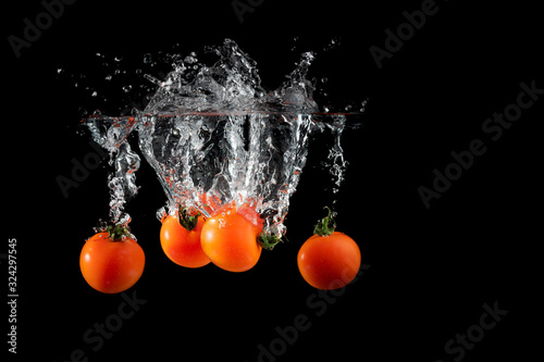 Cherry tomatoes isolated on black background falling into water with splash