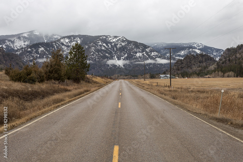 Empty roadway between grass fields leading to snow covered mountain range
