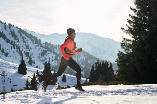 Trail runner in pink jacket woman running in winter mountains trail on snow.