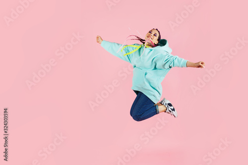 Beautiful young fit dancer in blue hoodie dancing and jumping isolated on pink background