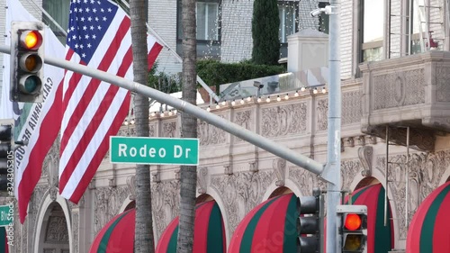 World famous Rodeo Drive Street Road Sign in Beverly Hills against American Unated States flag. Los Angeles, California, USA. Rich wealthy life consumerism, Luxury brands, high-class stores concept