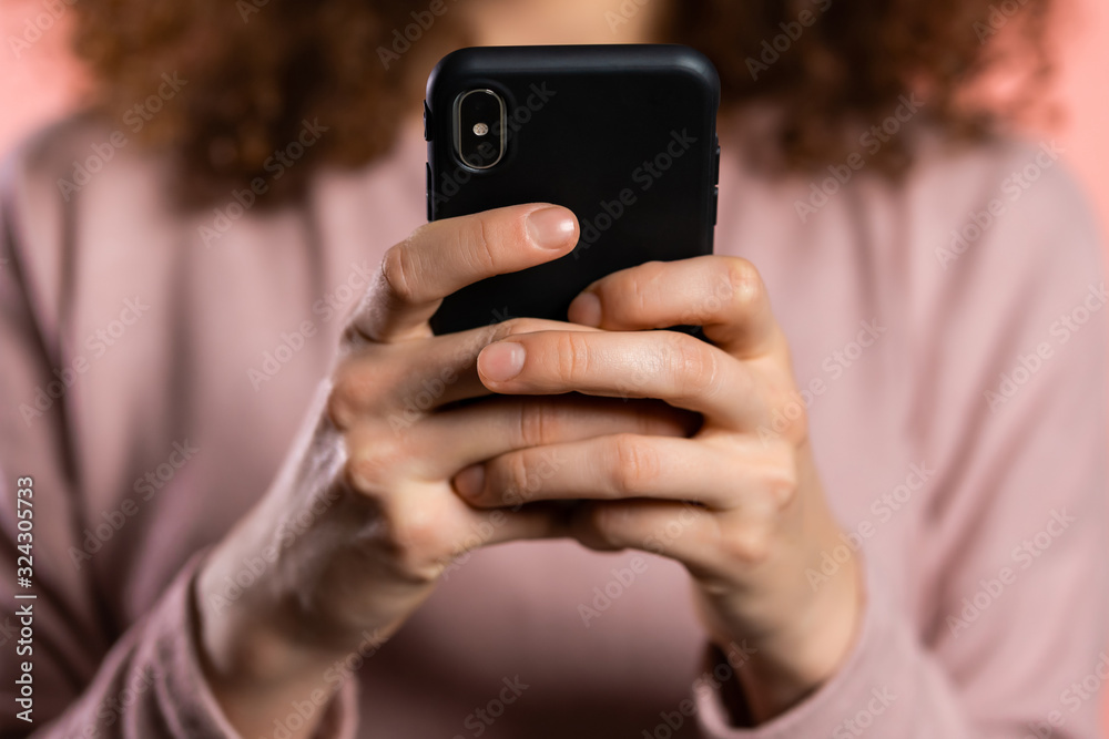 Hands of girl with curly hair using smartphone or surfing internet on pink studio background. Modern technology - apps, social networks Hands of girl with curly hair using smartphone or surfing internet on pink studio background. Modern technology - apps, social networks