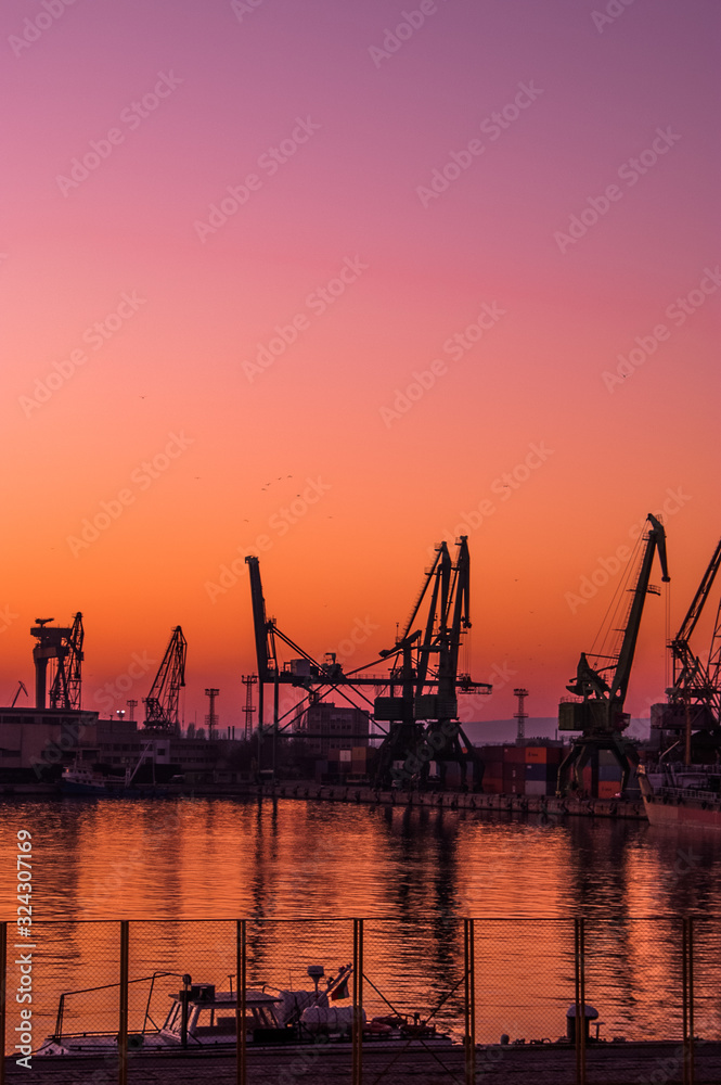 Sunset on cargo export and import port with cranes silhouette from industrial and transportation, trade port on business city