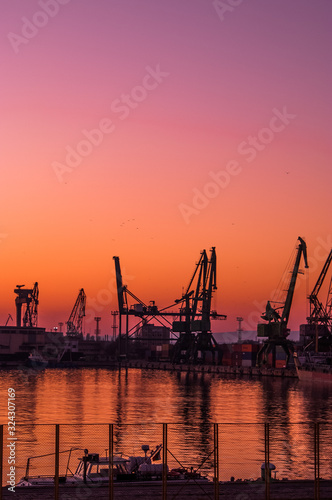Sunset on cargo export and import port with cranes silhouette from industrial and transportation  trade port on business city