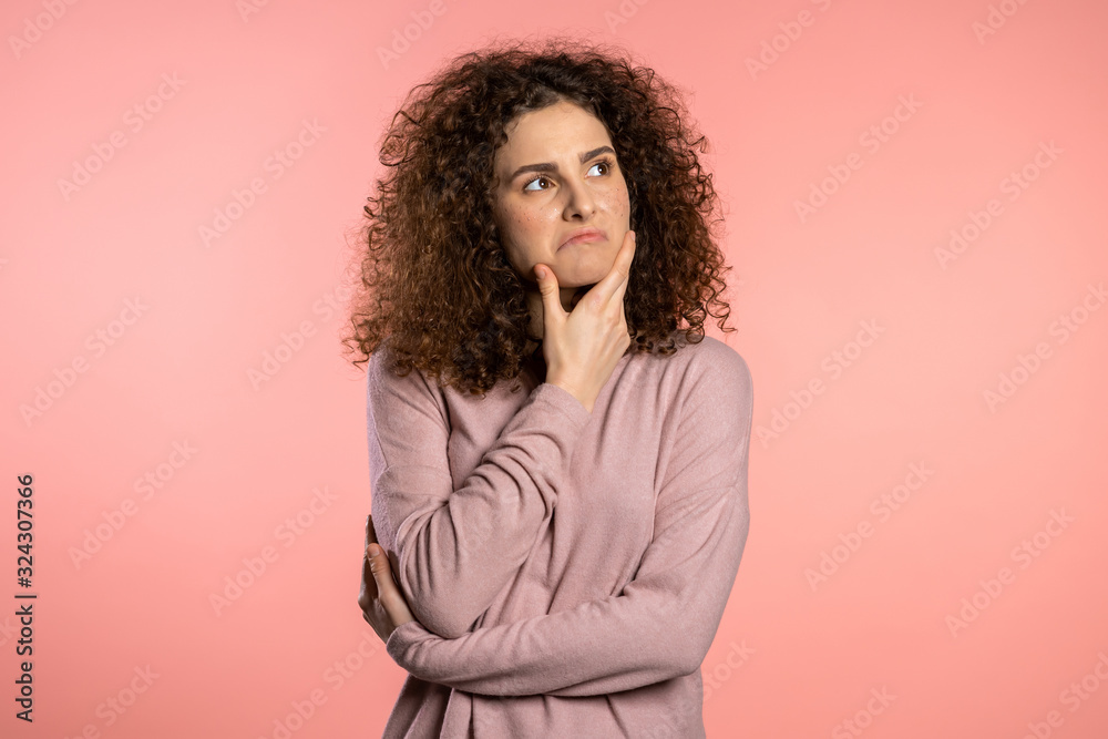Thinking woman looking up and around on pink background. Worried contemplative face expressions. Pretty curly girl model Thinking woman looking up and around on pink background. Worried contemplative face expressions. Pretty curly girl model
