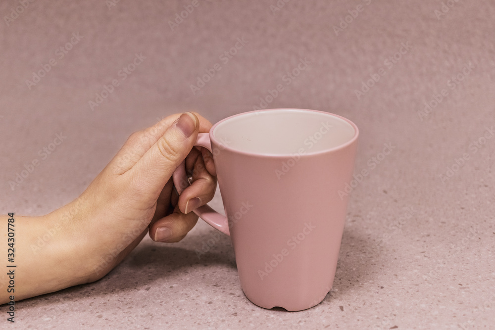 Pink cup in a female hand on a pink background Pink cup in a female hand on a pink background