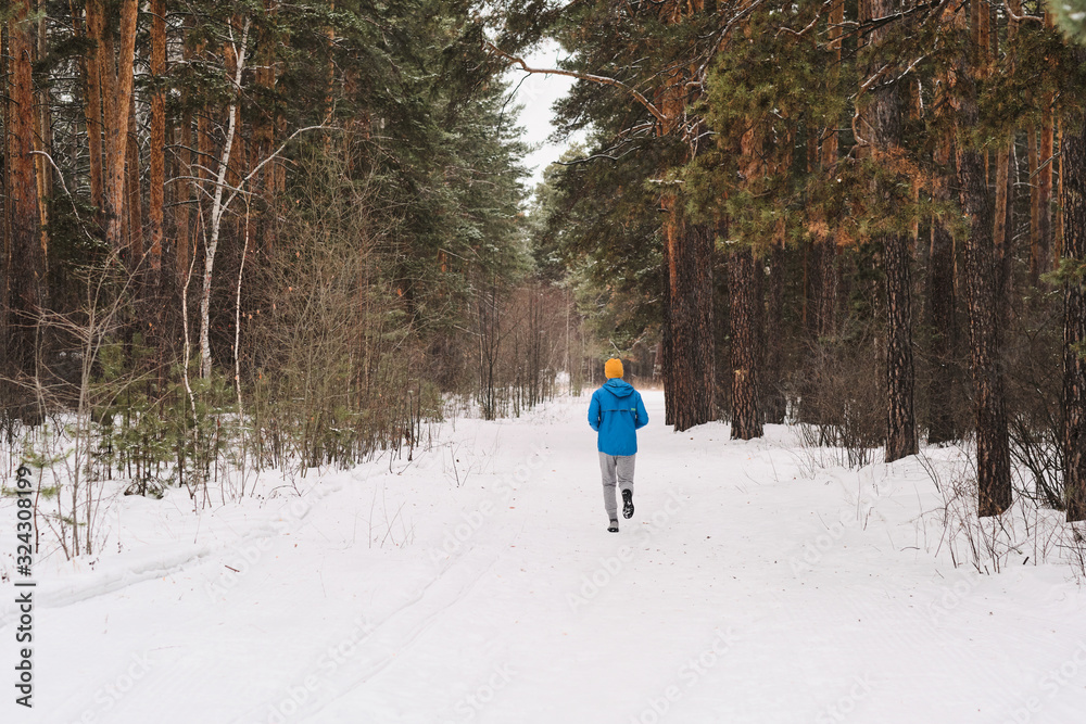 Rear view of unrecognizable man in blue jacket running in winter forest