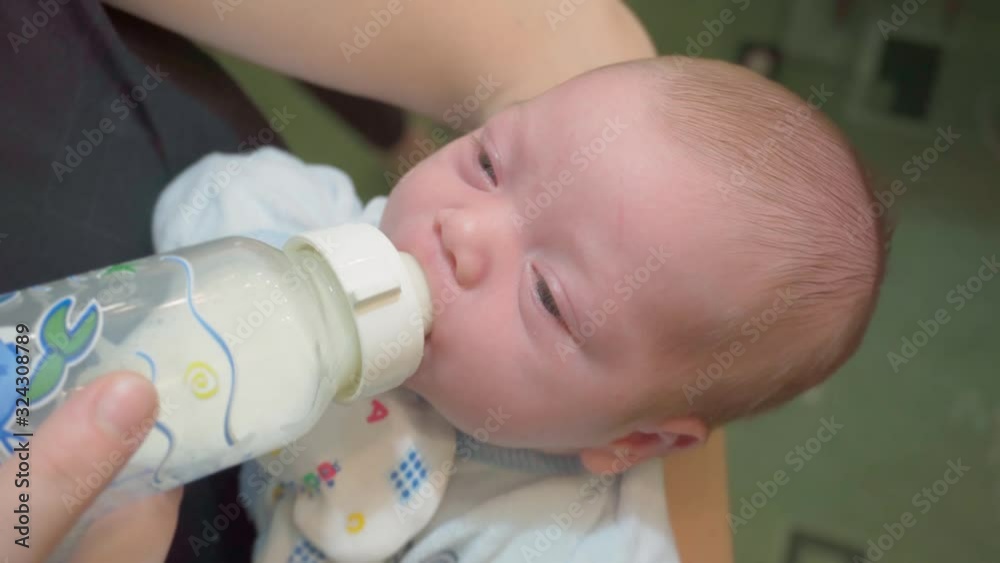 Portrait of cute newborn baby being fed by her mother using bottle. Loving woman giving to drink to her son. Mother feeding her baby. Portrait of cute newborn baby being fed by her mother using bottle. Loving woman giving to drink to her son. Mother feeding her baby.
