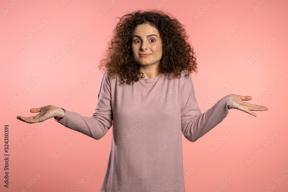 Ταπετσαρία Young curly unsure girl shrugs her arms, makes gesture of I don't know, care, can't help anything