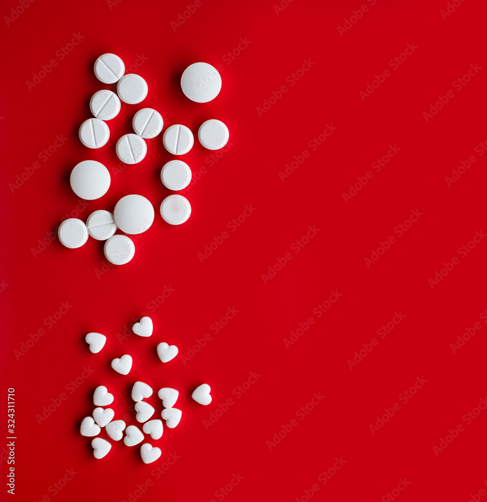 White large and small pills in the shape of a heart on a red background with empty place for text, top view White large and small pills in the shape of a heart on a red background with empty place for text, top view