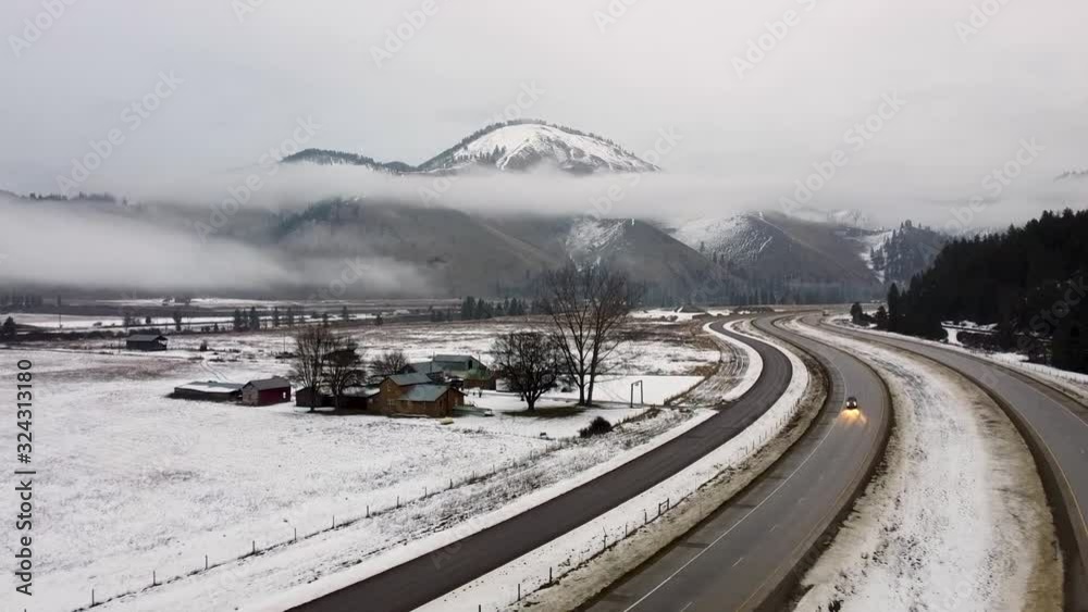 Overhead tracking shot of a snow covered ranch with mountain range and cars passing Overhead tracking shot of a snow covered ranch with mountain range and cars passing
