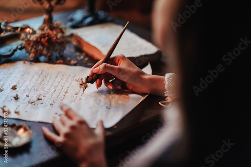 Girl writes a letter with an antique fountain pen. A female hand holds a pen over a sheet of paper in the light of a candle.