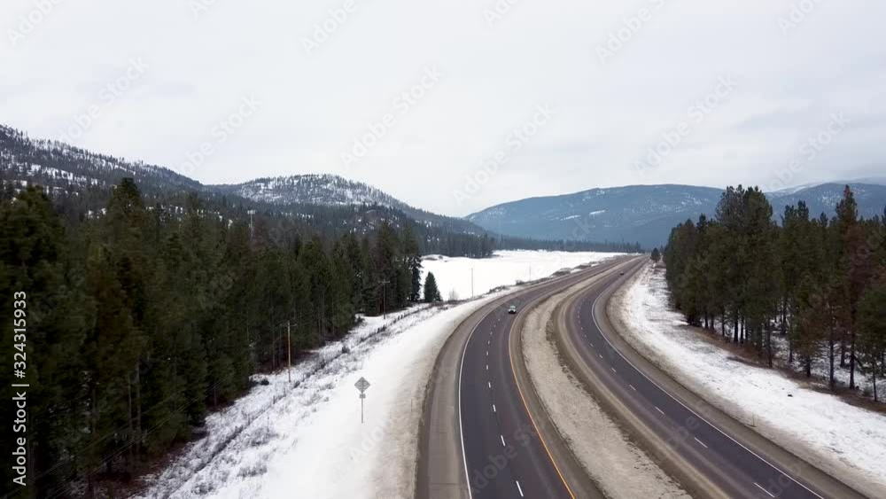 Reverse overhead shot with cars passing each other on the highway with snow, trees and mountain range Reverse overhead shot with cars passing each other on the highway with snow, trees and mountain range