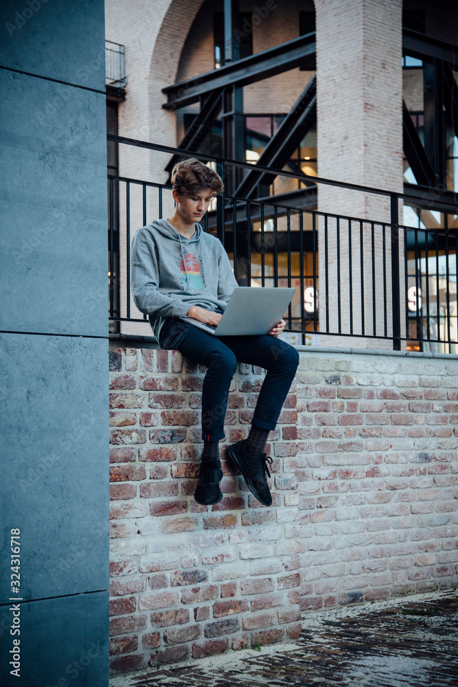 Teenager using laptop, sitting on a wall in the city Teenager using laptop, sitting on a wall in the city
