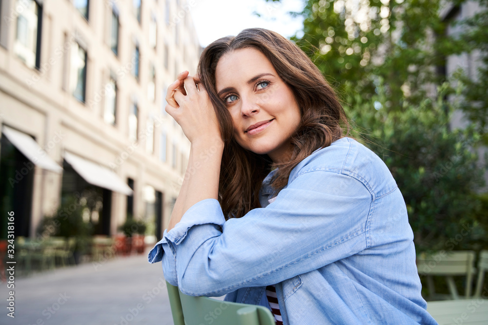 Portrait of smiling brunette woman sitting on a chair in the city Portrait of smiling brunette woman sitting on a chair in the city