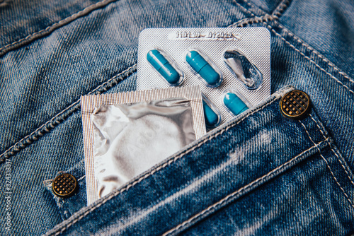 A pack of blue capsules in your pants pocket and a condom. Pills for men's health and sexual energy in jeans. Concept of erection, potency. Treatment of male infertility, impotence and prostatitis