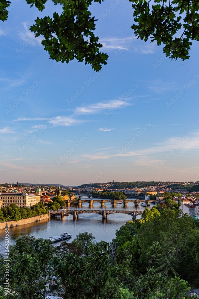 Prague / Czech Republic - May 23 2019: Scenic view of the cityscape, the river Vltava and Charles bridge, Manes and Jirasek bridges across water. Sunny spring evening with blue sky. Vertical image.
