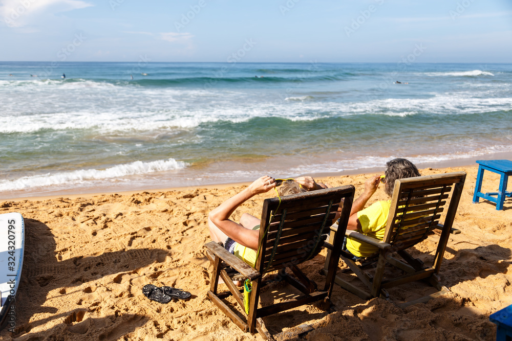 view from the back of an adult couple who are resting on sun beds near the sandy shore of ocean Asia, Sri Lanka view from the back of an adult couple who are resting on sun beds near the sandy shore of ocean Asia, Sri Lanka