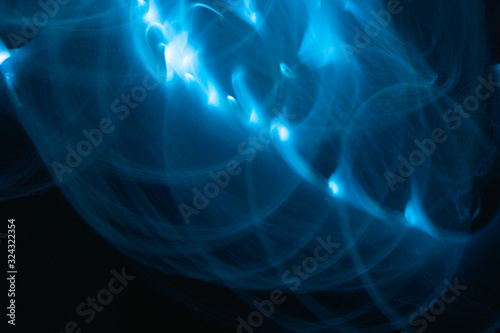 Neon blue light painting, long exposure photography, loop and swirl pattern against a black background. Abstract of blurred lighting equipment.