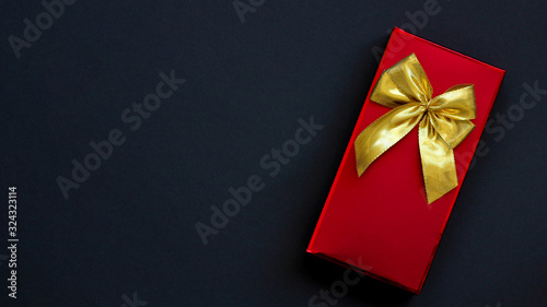 red box with a gold bow on a black background. The concept of a gift