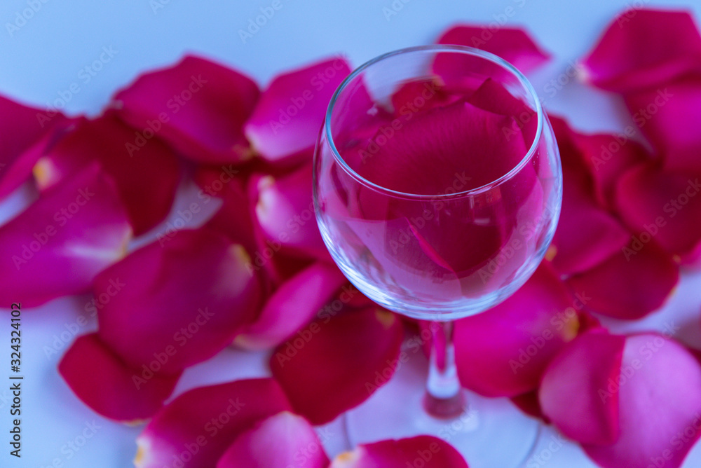 A glass of wine with rose petals inside. Everything is covered with rose petals. Pink and blue tones. Concept, love, loneliness, unrequited love. A glass of wine with rose petals inside. Everything is covered with rose petals. Pink and blue tones. Concept, love, loneliness, unrequited love.