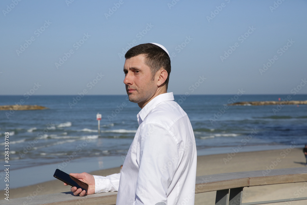 young jew businessman with mobile phone in hand on blue sea background young jew businessman with mobile phone in hand on blue sea background