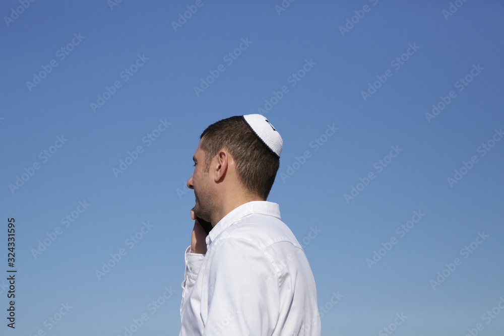 portrait of a young jew in kippah talking on a mobile phone on a blue sky background. Business concept.