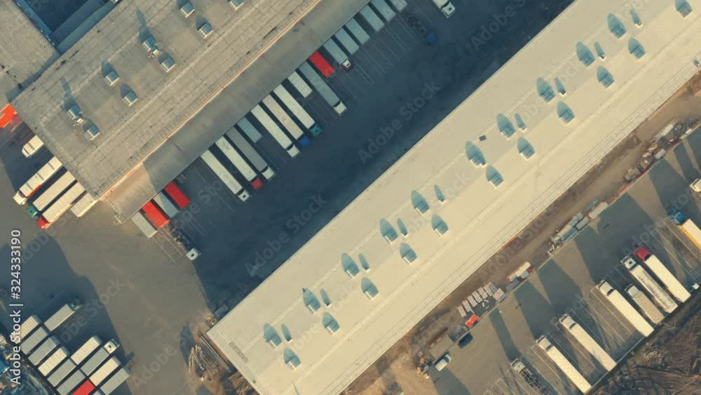 Aerial top down view of the logistics park with warehouse, loading hub with many semi trucks with cargo trailers standing at the ramps for load/unload goods Aerial top down view of the logistics park with warehouse, loading hub with many semi trucks with cargo trailers standing at the ramps for load/unload goods