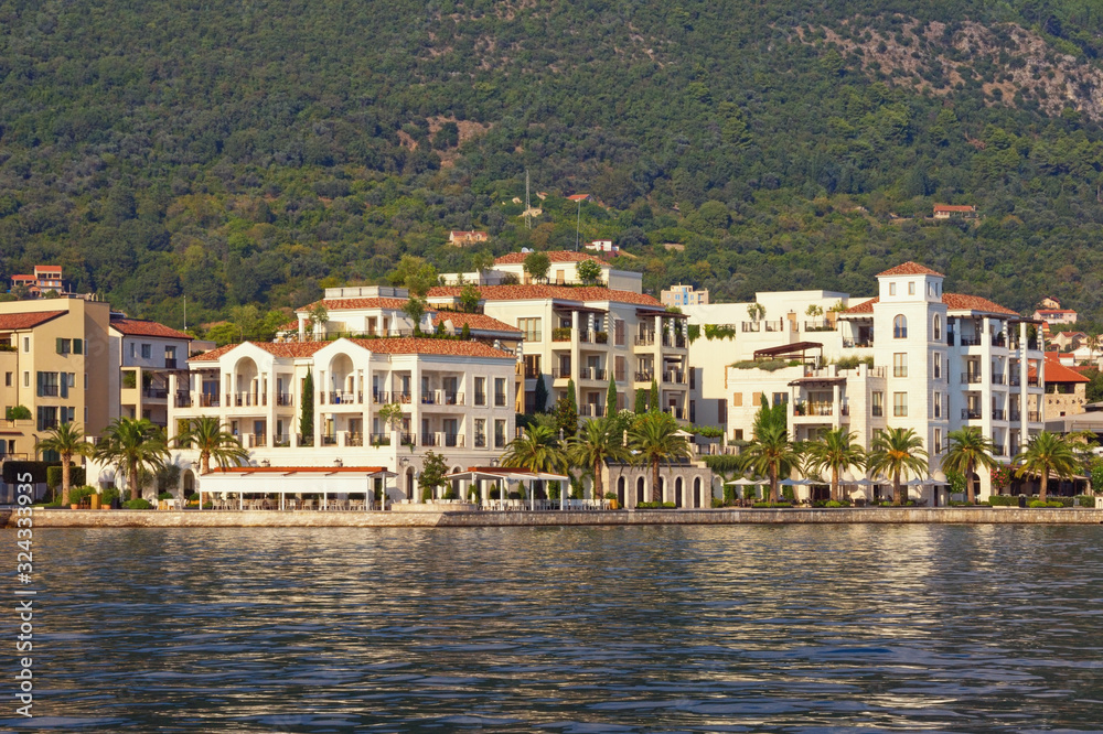 Mediterranean town at foot of mountain. Beautiful view of embankment of Tivat city from sea on sunny summer day. Montenegro, Adriatic Sea, Kotor Bay