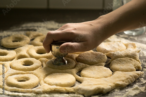 Woman making holes in raw homemade doughnuts pastry on the kitchen table, preparations for Fat Thursday holiday photo