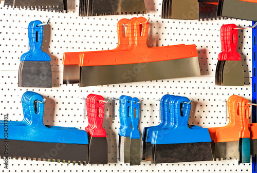 Spatulas, scrapers, trowels of various shapes and purposes hang on a metal stand. photo