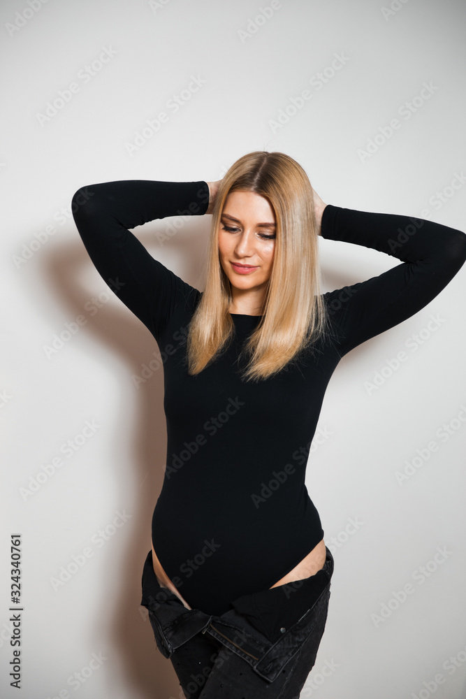 Fototapeta premium Beautiful glamour long hair woman posing for camera photographer wearing plack body with jeans - Portrait at a grey seamless background studio wall