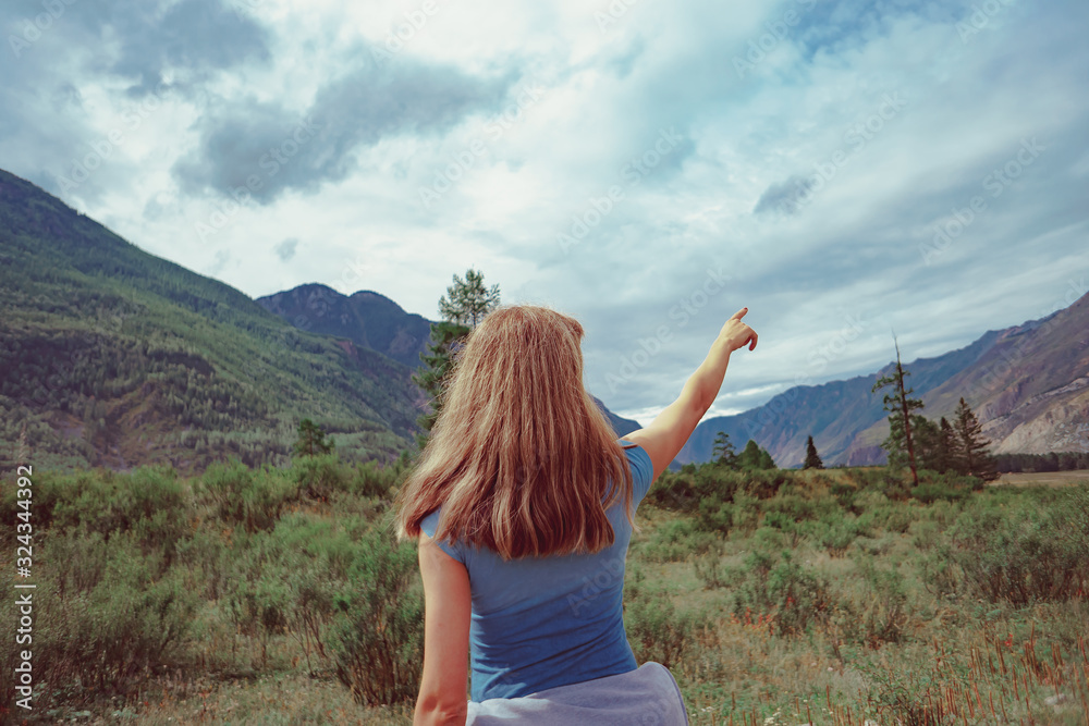 the girl stands with her back against the mountains