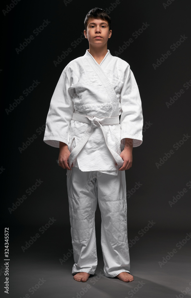 a teenager dressed in martial arts clothing poses on a dark gray background, a sports concept a teenager dressed in martial arts clothing poses on a dark gray background, a sports concept