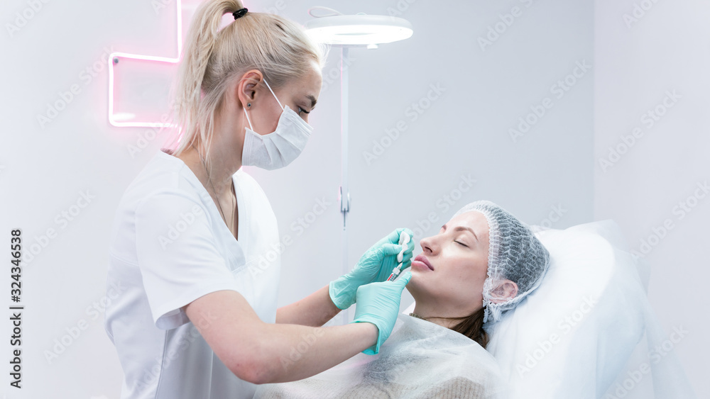 Obraz premium The young beautician doctor preparing to making injection in female lips. The doctor cosmetologist makes lip augmentation procedure.
