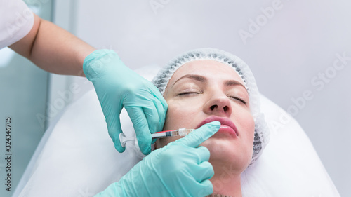 The young beautician doctor preparing to making injection in female lips. The doctor cosmetologist makes lip augmentation procedure.
