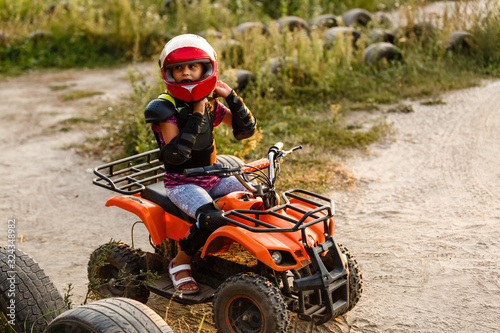 The little girl rides a quad bike ATV. A mini quad bike is a cool girl in a helmet and protective clothing. Electric quad bike electric car for children popularizes green technology.